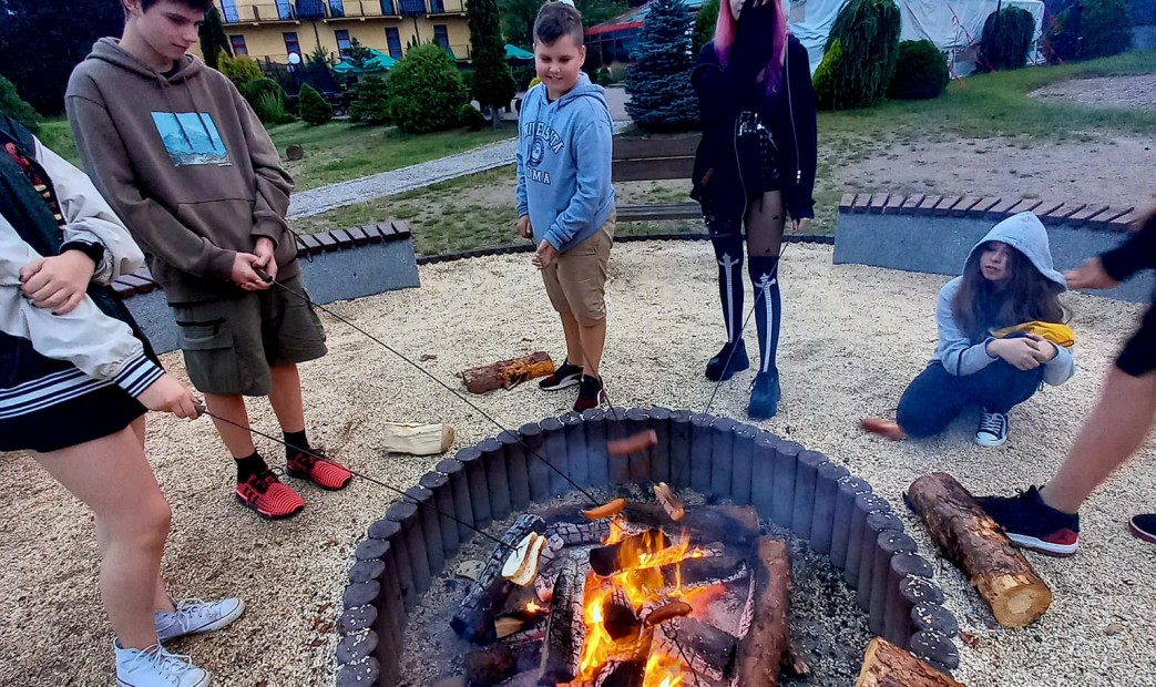 Dzieci i młodzież piecze kiełbaski na ognisku